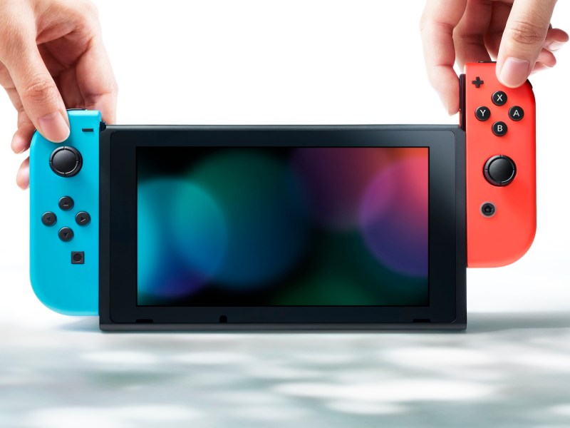 Eine Nintendo Switch mit einem roten und blauen Joy-Con und zwei Händen.